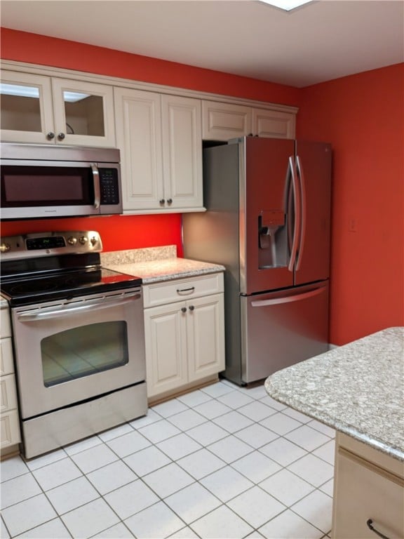 kitchen with stainless steel appliances, light tile floors, white cabinetry, and light stone counters