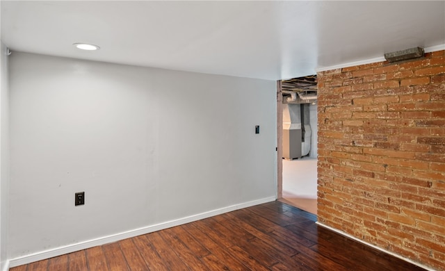 spare room with dark wood-type flooring and brick wall