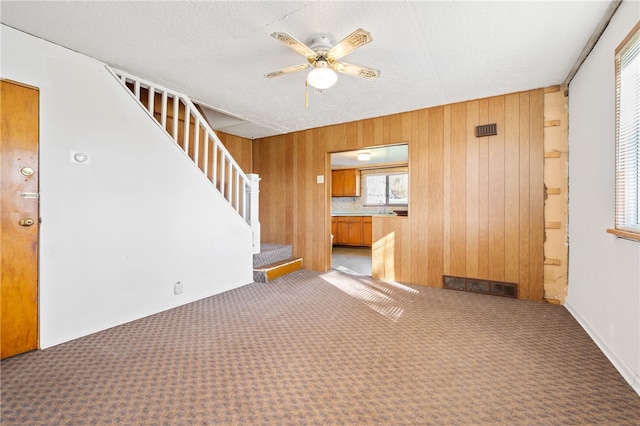 spare room with ceiling fan, dark colored carpet, and wooden walls