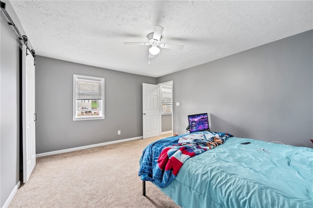 bedroom featuring ceiling fan, light colored carpet, a barn door, and a textured ceiling