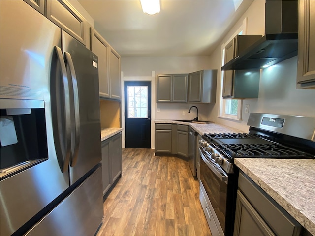 kitchen featuring appliances with stainless steel finishes, a healthy amount of sunlight, wall chimney exhaust hood, and light hardwood / wood-style flooring