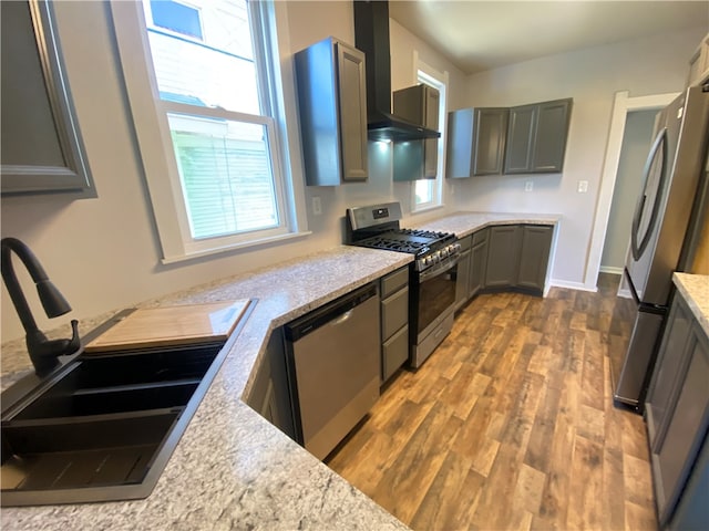 kitchen with appliances with stainless steel finishes, wall chimney range hood, dark wood-type flooring, and sink