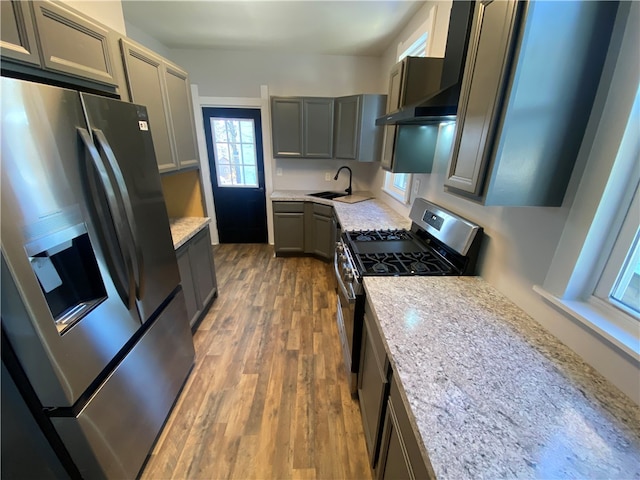 kitchen with light stone countertops, appliances with stainless steel finishes, gray cabinets, wood-type flooring, and sink