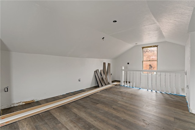 additional living space featuring dark wood-type flooring, vaulted ceiling, and a textured ceiling