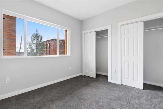 unfurnished bedroom with two closets and dark colored carpet