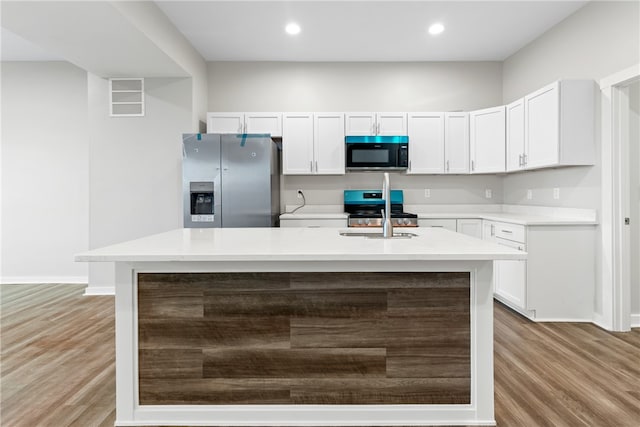 kitchen with white cabinetry, appliances with stainless steel finishes, light wood-type flooring, and a kitchen island with sink