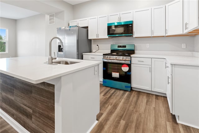 kitchen with appliances with stainless steel finishes, white cabinetry, hardwood / wood-style flooring, and an island with sink