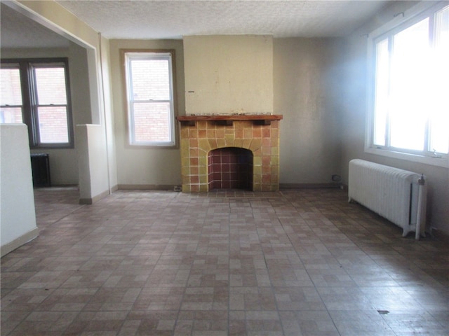 unfurnished living room featuring radiator, a textured ceiling, a healthy amount of sunlight, and tile floors