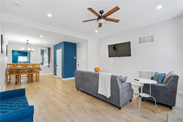 living room with ceiling fan with notable chandelier and light hardwood / wood-style flooring