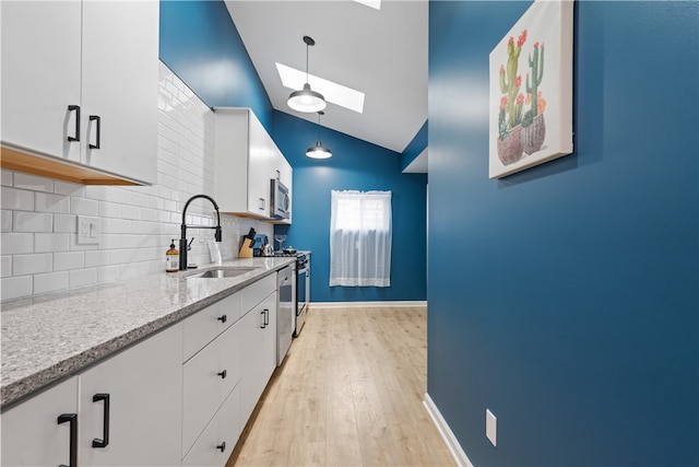 kitchen featuring appliances with stainless steel finishes, white cabinets, light hardwood / wood-style floors, backsplash, and vaulted ceiling with skylight