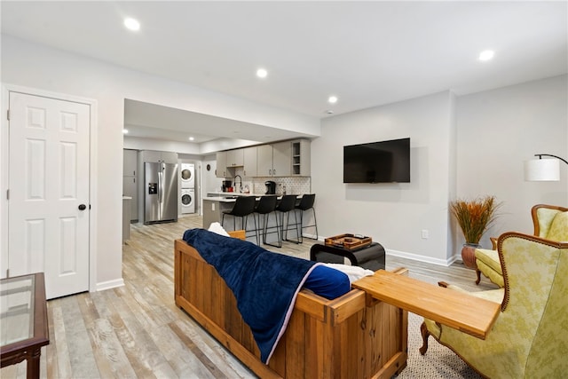 living room with light hardwood / wood-style floors, stacked washer and dryer, and sink