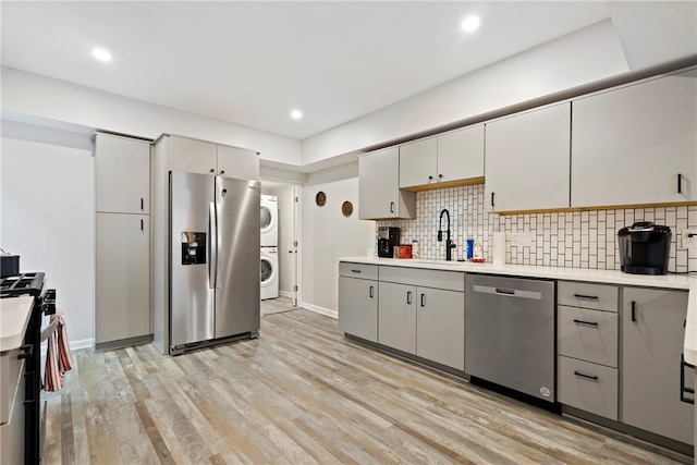 kitchen featuring appliances with stainless steel finishes, sink, light hardwood / wood-style floors, backsplash, and stacked washing maching and dryer