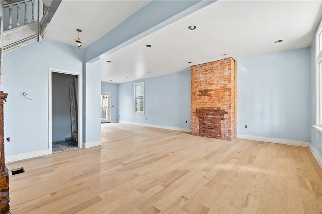 unfurnished living room with brick wall and light wood-type flooring