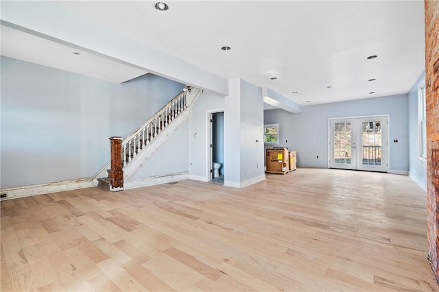 unfurnished living room featuring french doors, light hardwood / wood-style floors, and brick wall