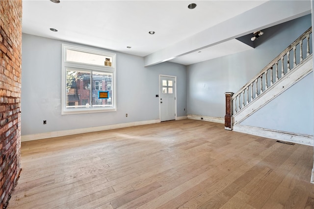 unfurnished living room featuring brick wall and light hardwood / wood-style flooring