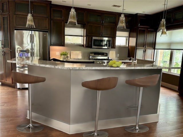 kitchen with appliances with stainless steel finishes, an island with sink, light hardwood / wood-style flooring, and decorative light fixtures