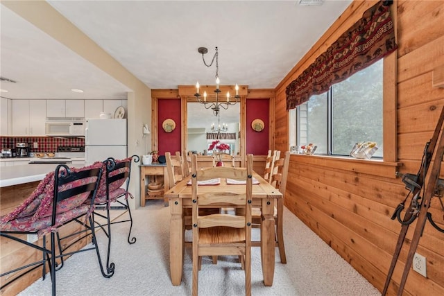 dining space with an inviting chandelier, light colored carpet, and wooden walls