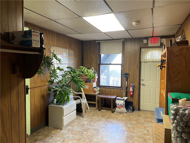 misc room with a drop ceiling, wood walls, and light tile floors