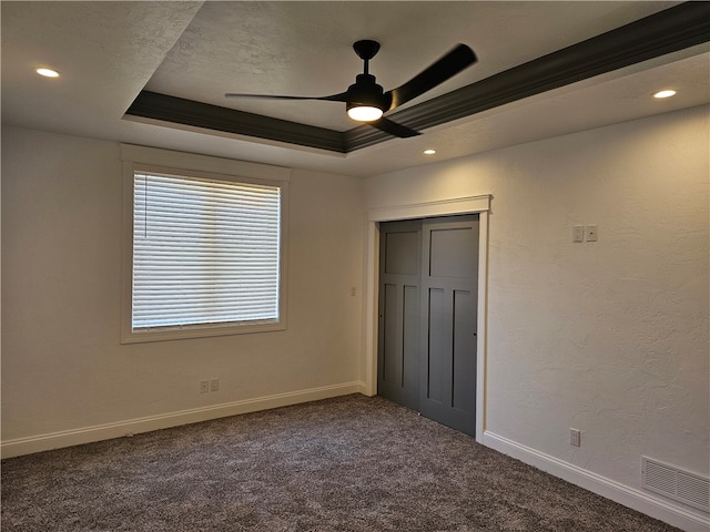 unfurnished bedroom with a closet, a tray ceiling, dark carpet, and ceiling fan