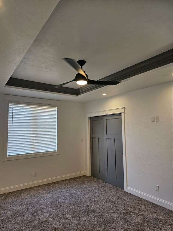 unfurnished bedroom featuring ceiling fan, dark colored carpet, a closet, and a tray ceiling