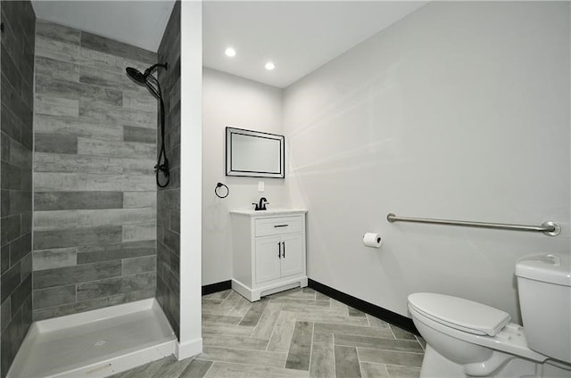 bathroom featuring toilet, vanity, a tile shower, and parquet flooring