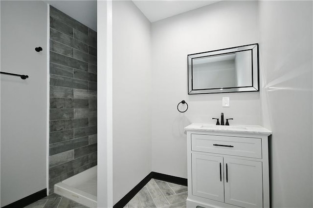 bathroom with wood-type flooring, tiled shower, and vanity