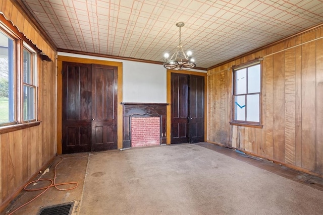 carpeted empty room with a healthy amount of sunlight, a notable chandelier, crown molding, and wooden walls