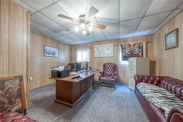 carpeted office with wooden walls, a drop ceiling, and ceiling fan