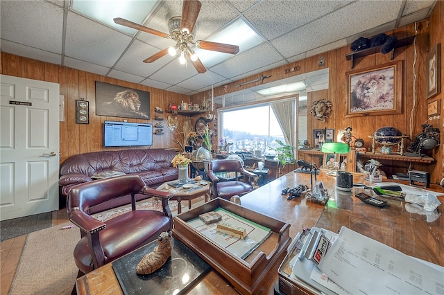 living room featuring wood walls, ceiling fan, and a paneled ceiling