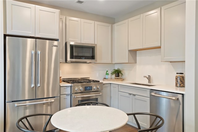 kitchen with wood-type flooring, sink, high end appliances, and white cabinetry