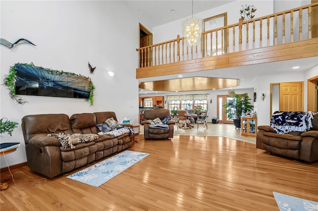 living room with a notable chandelier, light wood-type flooring, and a high ceiling