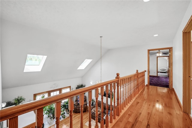 hall with high vaulted ceiling, an inviting chandelier, a skylight, and light wood-type flooring