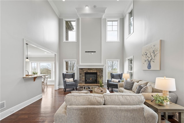 living room featuring ornamental molding, dark hardwood / wood-style flooring, a high ceiling, and a stone fireplace