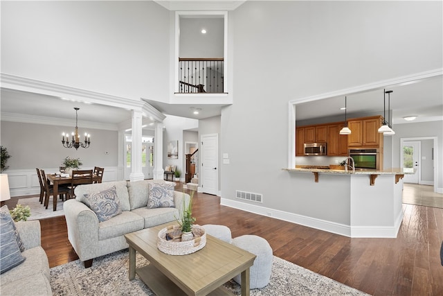 living room featuring crown molding, wood-type flooring, a notable chandelier, and decorative columns