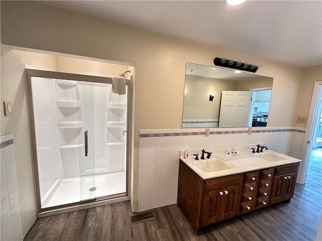 bathroom with a shower with shower door, double vanity, tile walls, and hardwood / wood-style floors