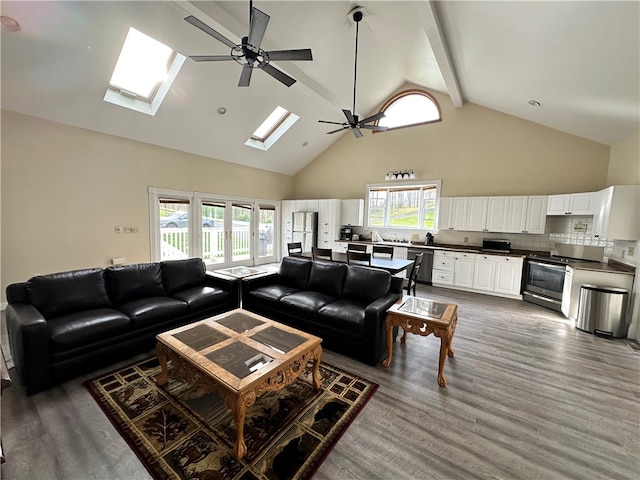 living room with a skylight, dark hardwood / wood-style floors, high vaulted ceiling, and ceiling fan