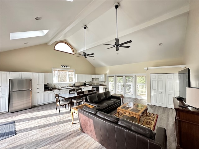 living room featuring a healthy amount of sunlight, light wood-type flooring, beam ceiling, a skylight, and ceiling fan