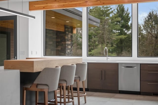 bar featuring light tile patterned flooring, dishwasher, dark brown cabinetry, and sink