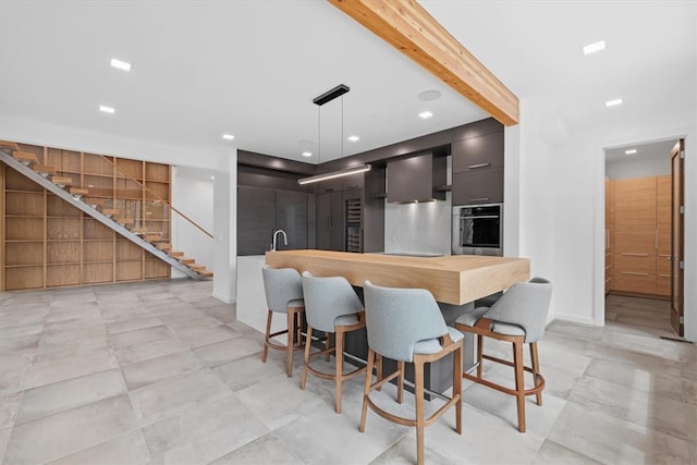 kitchen with pendant lighting, wall chimney exhaust hood, beamed ceiling, oven, and light tile patterned floors