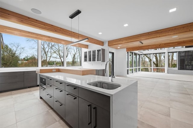 kitchen with gray cabinets, hanging light fixtures, a center island with sink, and sink