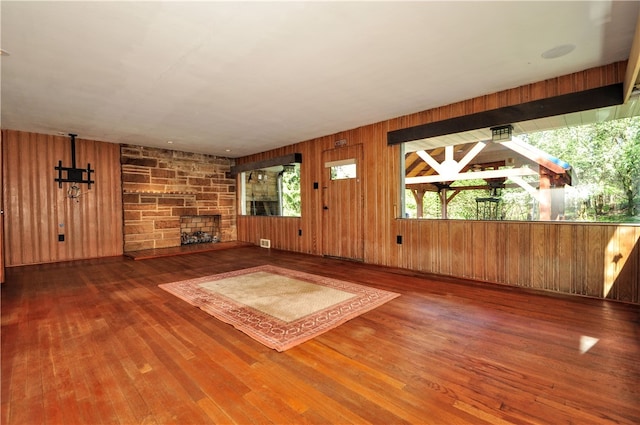 unfurnished living room with wood walls, dark wood-type flooring, and a stone fireplace