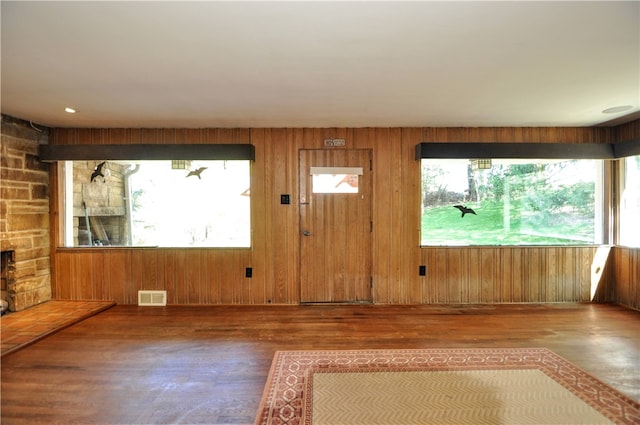 entrance foyer with dark wood-type flooring, wooden walls, and a stone fireplace