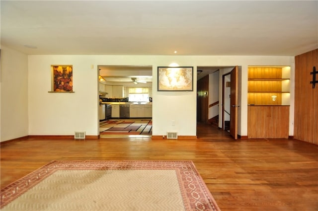 unfurnished living room featuring wood-type flooring, ceiling fan, and built in shelves