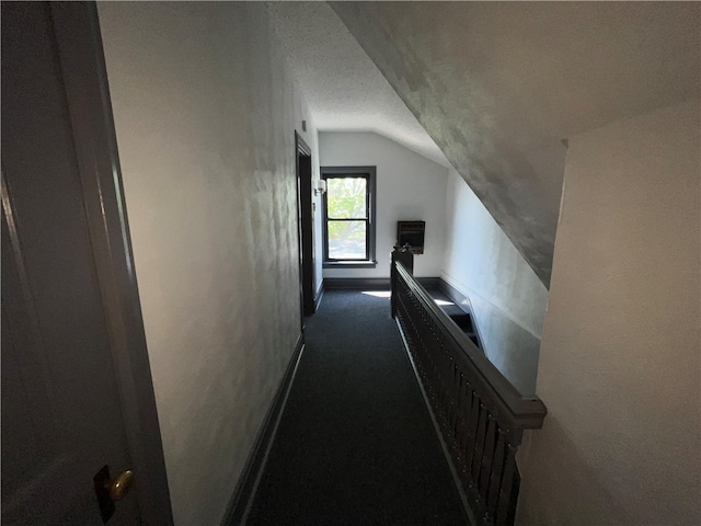 corridor featuring a textured ceiling, vaulted ceiling, and dark colored carpet