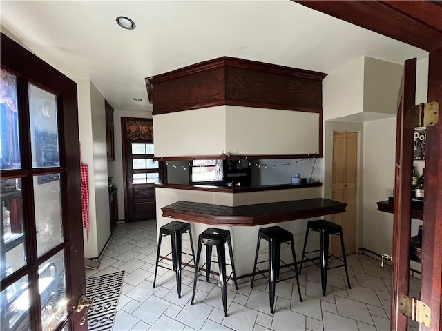 kitchen with a kitchen breakfast bar, kitchen peninsula, fridge, and light tile flooring