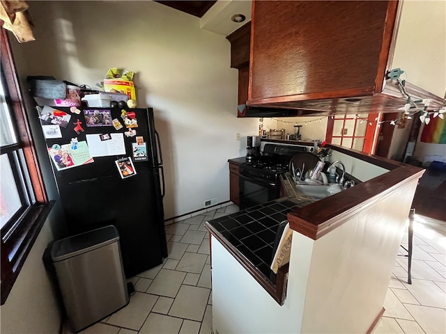 kitchen with tile counters, a breakfast bar area, light tile floors, and black appliances