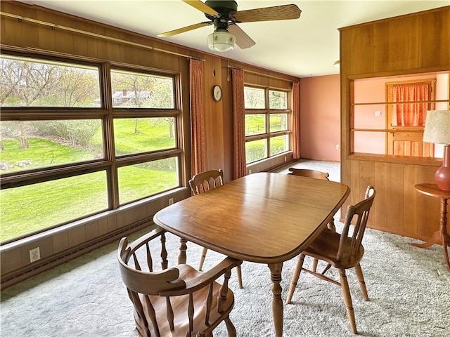 carpeted dining space featuring wood walls and ceiling fan