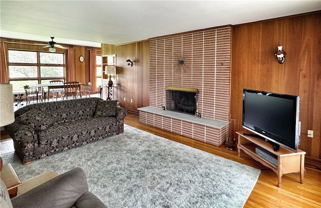 living room featuring wood walls, a fireplace, brick wall, light hardwood / wood-style floors, and ceiling fan