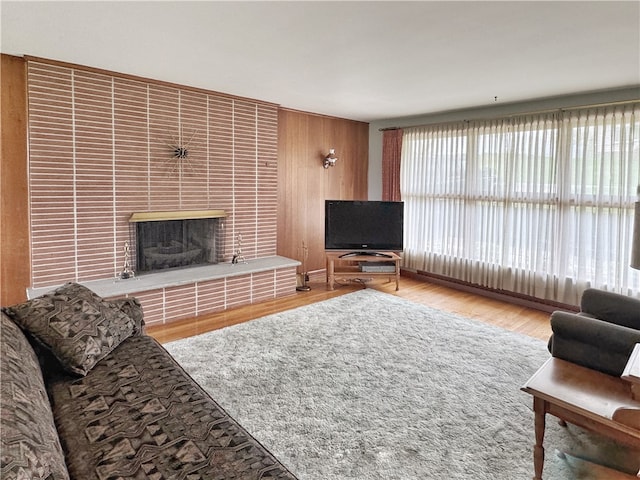 living room with wooden walls, light hardwood / wood-style floors, and a brick fireplace