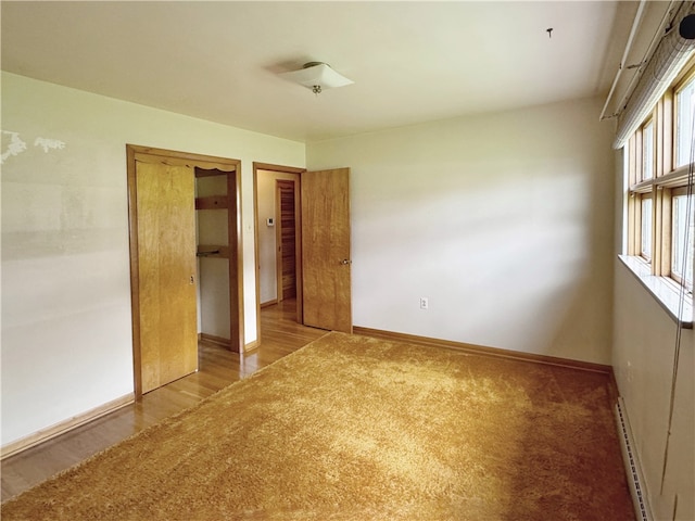 unfurnished bedroom featuring a baseboard heating unit, light hardwood / wood-style flooring, a closet, and multiple windows